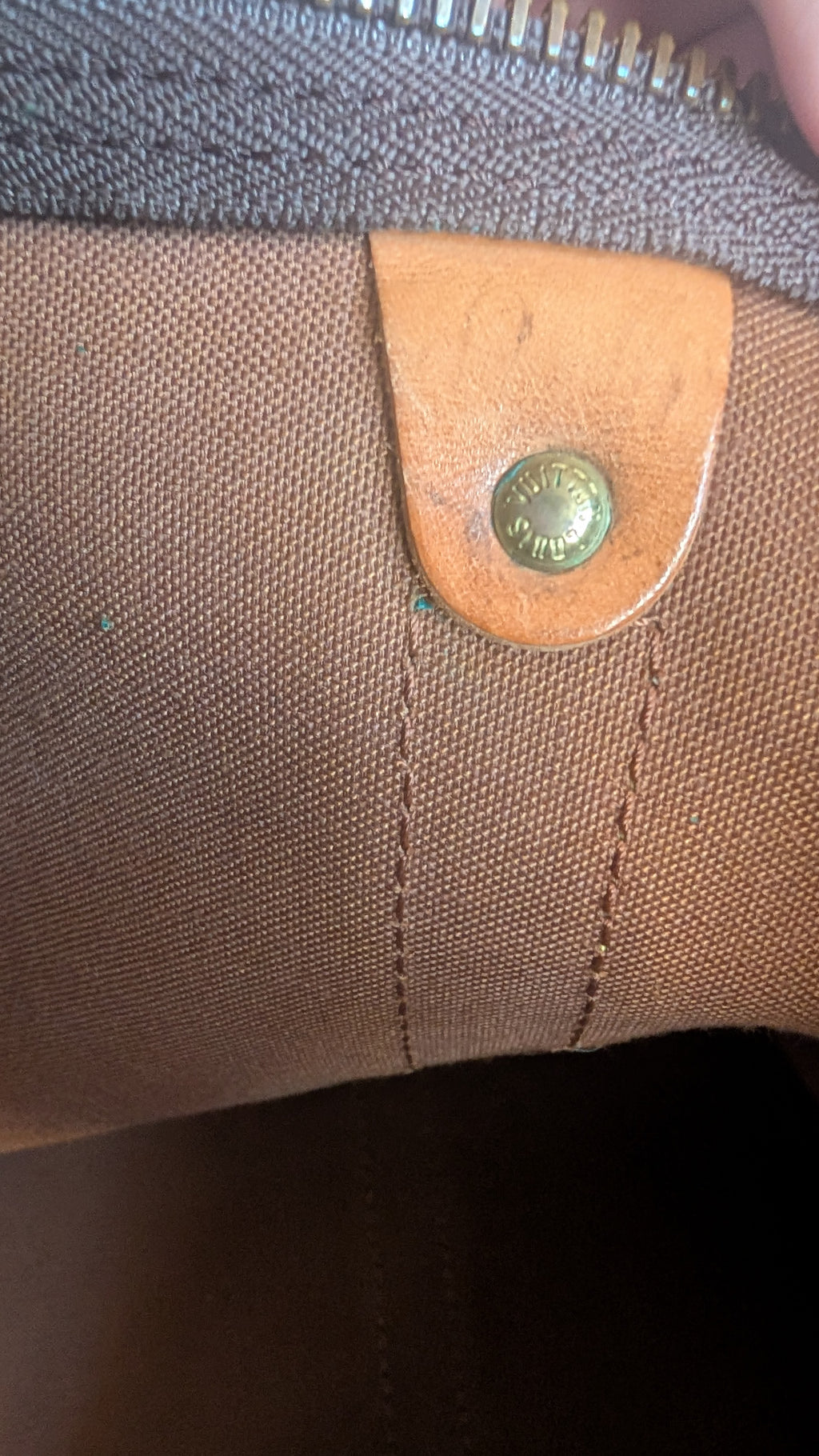 Close-up of a brown canvas bag with a tan leather tab and a brass snap button, showing the texture of the materials. Pre-Owned Louis Vuitton Keepall Bandoulière 60 Monogram Travel Bag