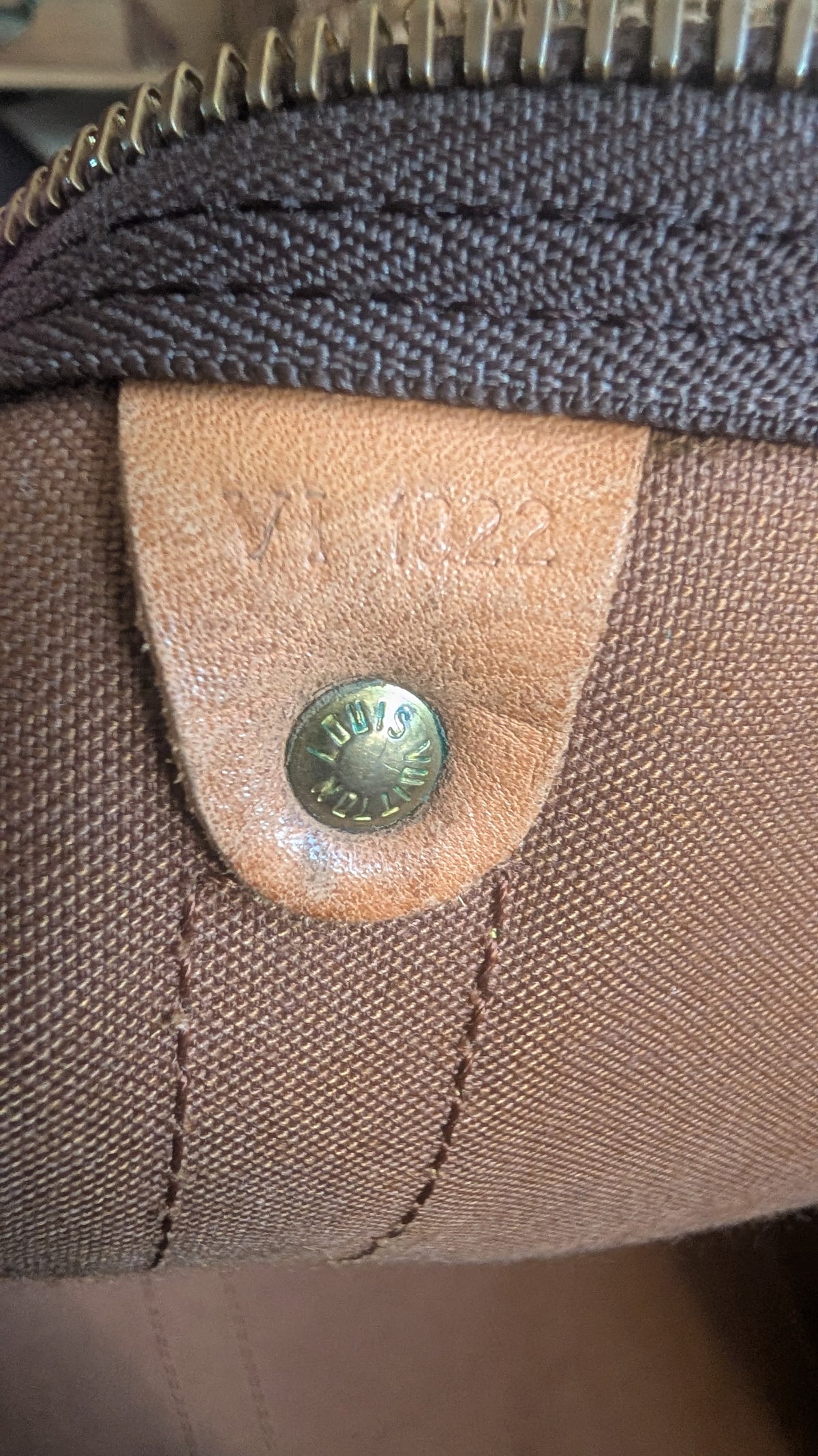 Close-up of a Louis Vuitton canvas bag showing the interior lining, a tan leather tab stamped with 'LV 1223', and a brass snap button closure. Pre-Owned Louis Vuitton Keepall Bandoulière 60 Monogram Travel Bag