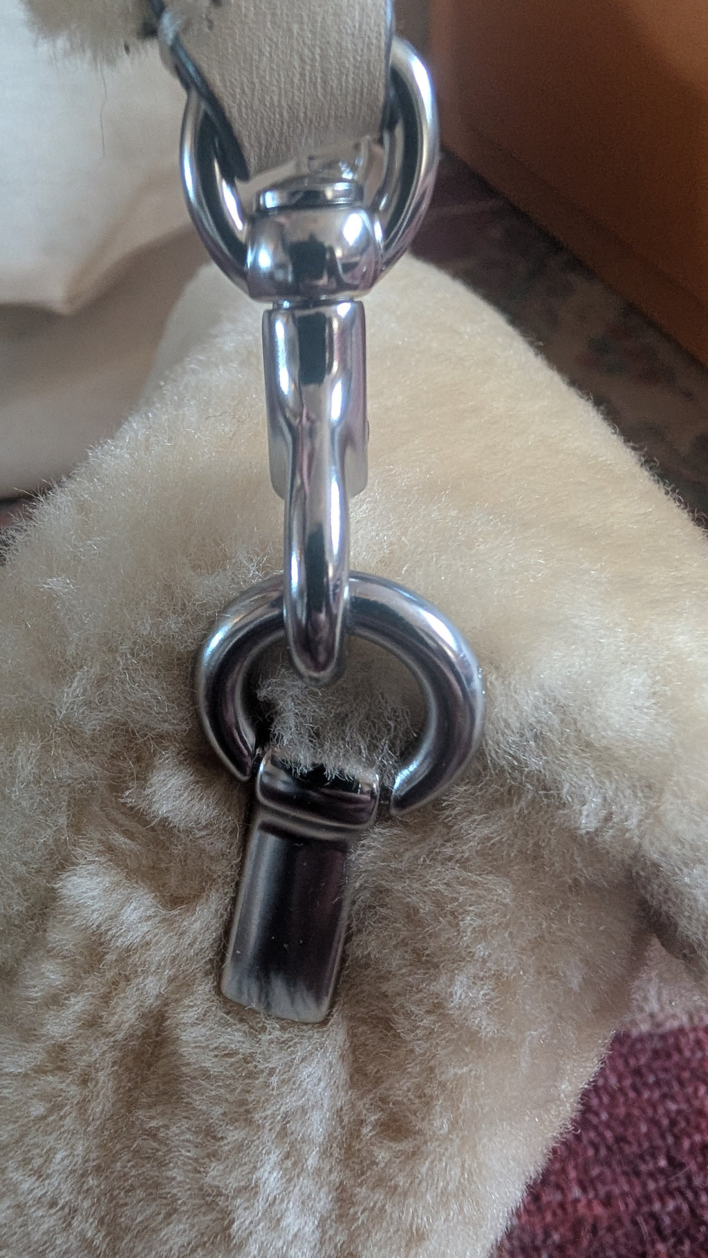 Close-up of a polished silver-tone metal hardware clasp and D-ring attached to a light beige textured strap, resting on a fluffy cream-colored surface. Pre-Owned Coach Tabby 18 Shearling Shoulder / Crossbody Bag – Cream