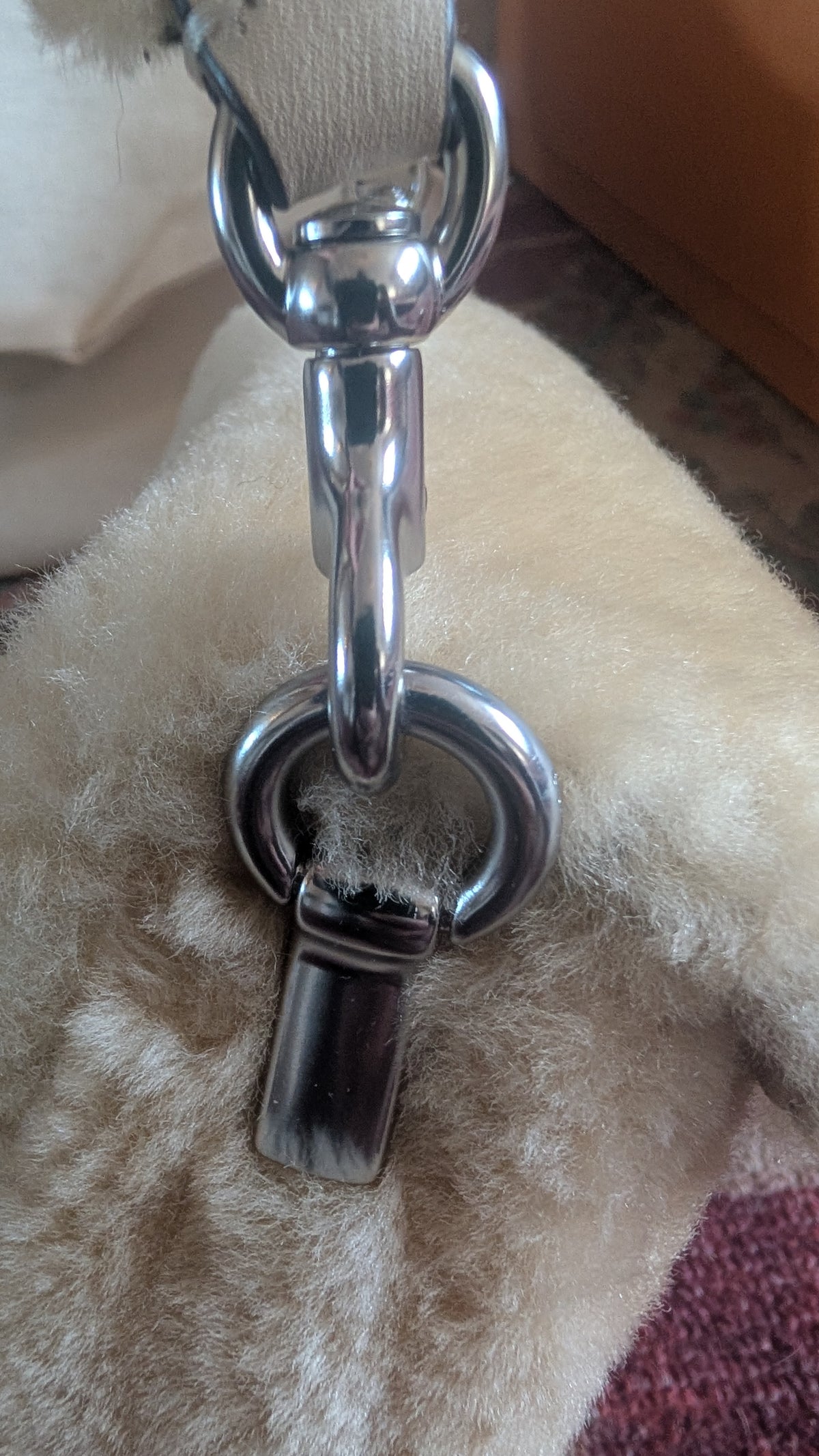 Close-up of a polished silver-tone metal hardware clasp and D-ring attached to a light beige textured strap, resting on a fluffy cream-colored surface. Pre-Owned Coach Tabby 18 Shearling Shoulder / Crossbody Bag – Cream