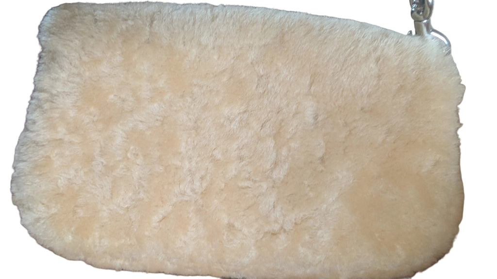 A cream-colored faux-shearling or sheepskin clutch bag with a silver metal clasp, resting on a patterned red and beige fabric surface. Pre-Owned Coach Tabby 18 Shearling Shoulder / Crossbody Bag – Cream