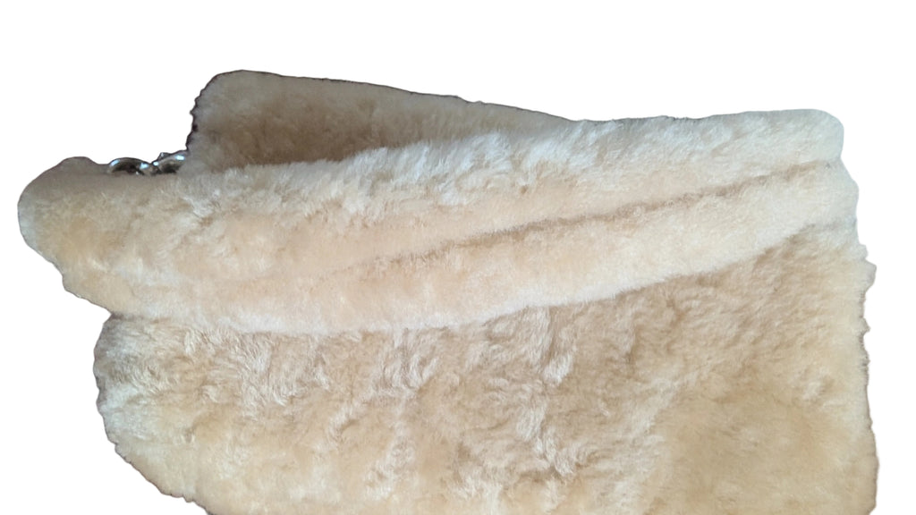 A cream-colored faux fur clutch or pouch with a soft, fluffy texture, resting on a patterned rug next to a white surface. Pre-Owned Coach Tabby 18 Shearling Shoulder / Crossbody Bag – Cream