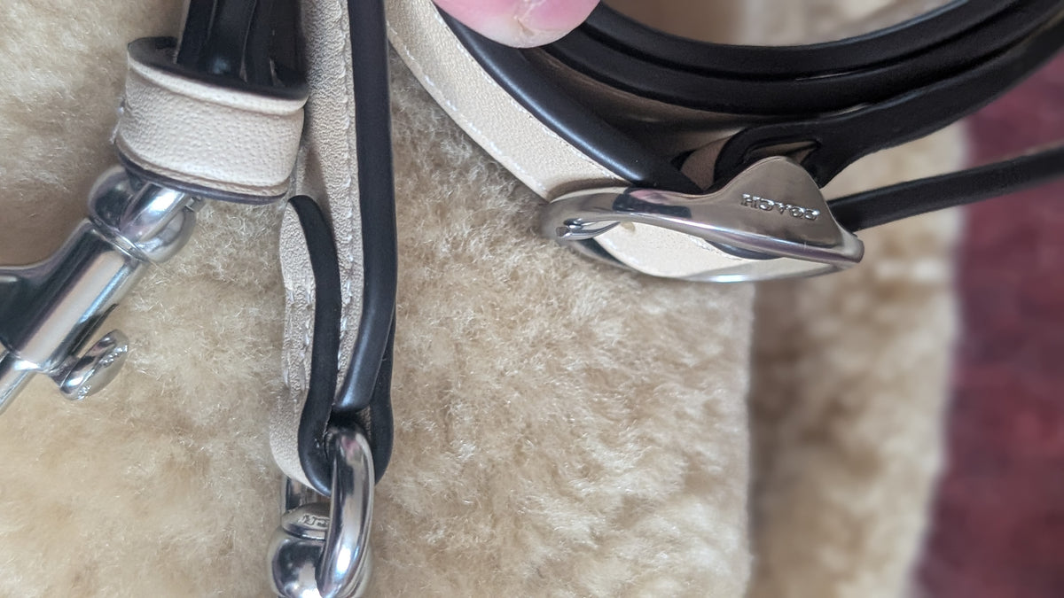Close-up of a Coach leather strap with a silver-tone metal buckle and hardware, resting on a beige textured surface. Pre-Owned Coach Tabby 18 Shearling Shoulder / Crossbody Bag – Cream