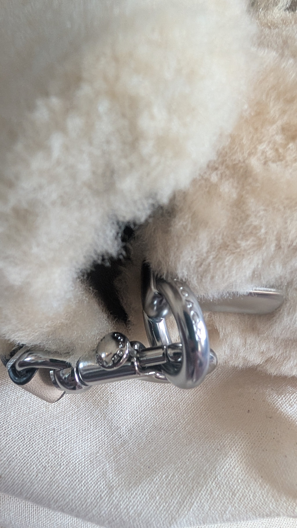 Close-up of a cream-colored sheepskin or faux-shearling bag with a polished silver-tone metal horsebit clasp. Pre-Owned Coach Tabby 18 Shearling Shoulder / Crossbody Bag – Cream