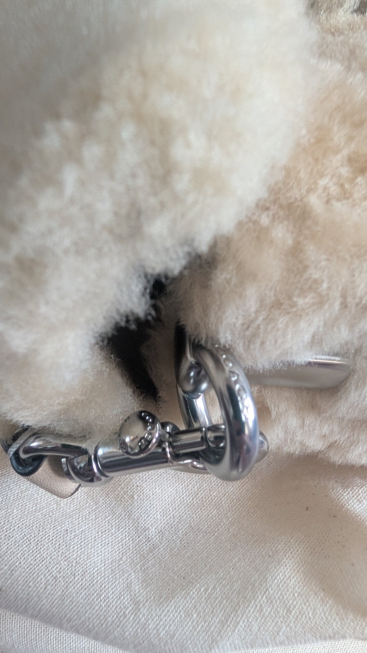 Close-up of a cream-colored sheepskin or faux-shearling bag with a polished silver-tone metal horsebit clasp. Pre-Owned Coach Tabby 18 Shearling Shoulder / Crossbody Bag – Cream
