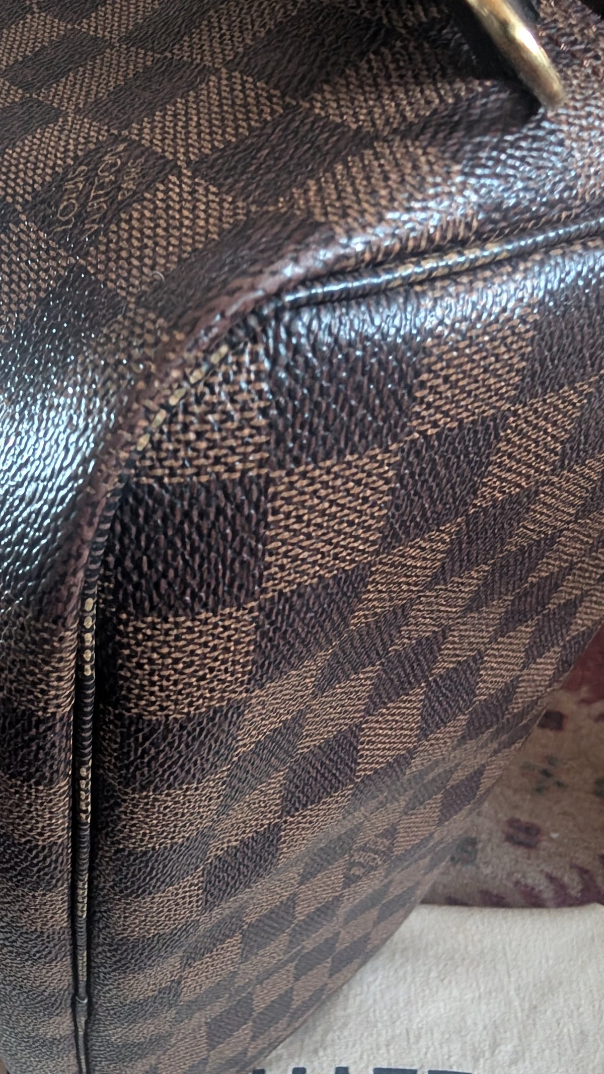 Close-up of a brown and beige checkered patterned leather bag with a visible zipper and a small gold metal  Pre-Owned Louis Vuitton Neverfull MM Damier Ebene, Cerise Redaccent. Pre-Owned Louis Vuitton Neverfull MM Damier Ebene, Cerise Red