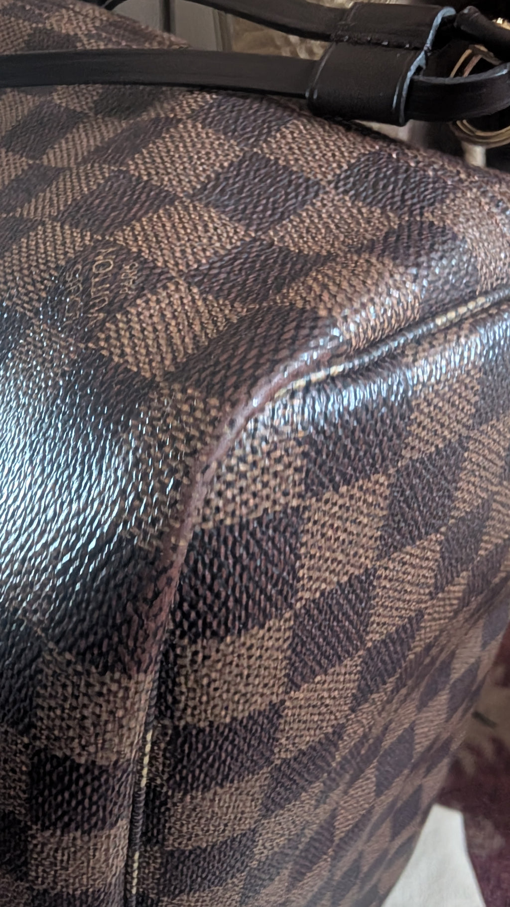 Close-up of a brown and beige checkered patterned leather bag with a black strap and a faint embossed brand  Pre-Owned Louis Vuitton Neverfull MM Damier Ebene, Cerise Redlogo.