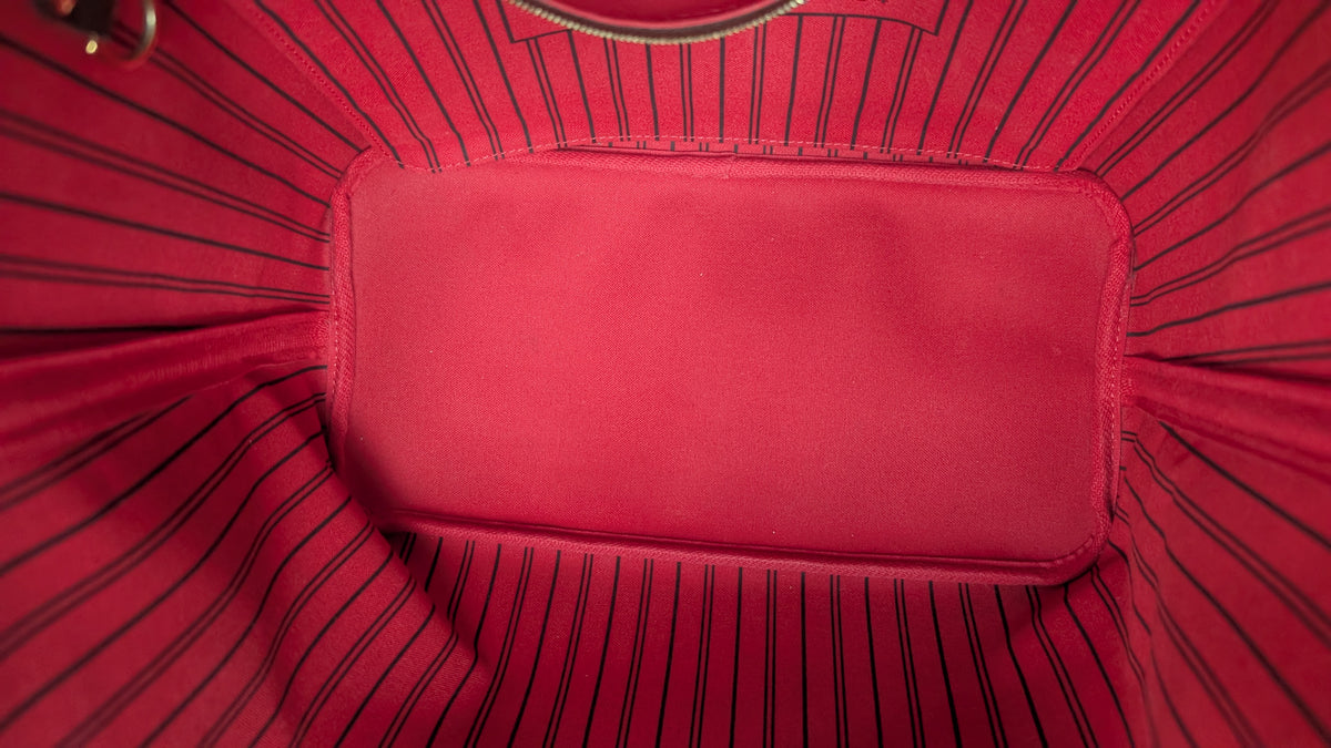 Close-up of the interior lining of a red tote bag, showing a smooth rectangular pocket centered on a red fabric background with thin black pinstripes. Pre-Owned Louis Vuitton Neverfull MM Damier Ebene, Cerise Red