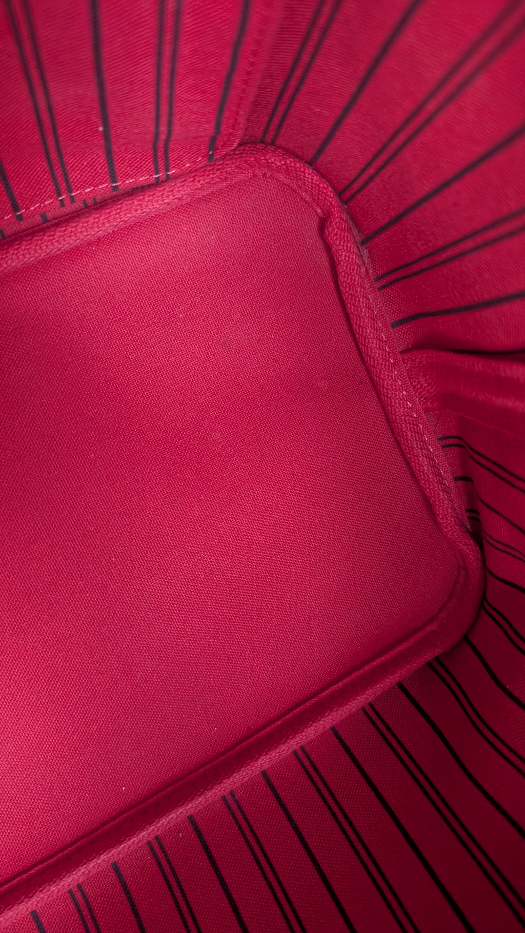 Close-up of a bright pink fabric product with black pinstripes and a stitched corner detail. Pre-Owned Louis Vuitton Neverfull MM Damier Ebene, Cerise Red
