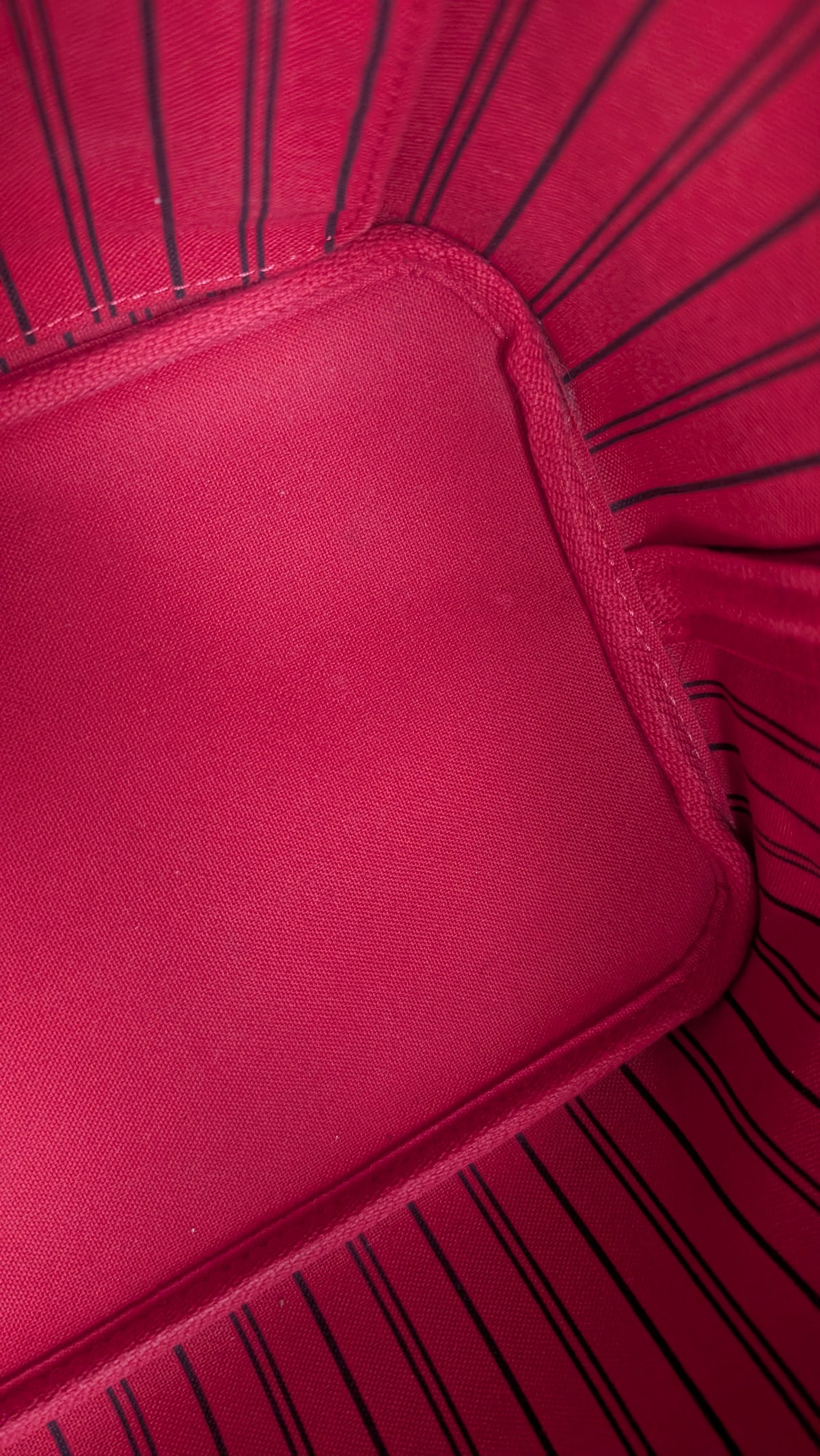 Close-up of a bright pink fabric product with black pinstripes and a stitched corner detail. Pre-Owned Louis Vuitton Neverfull MM Damier Ebene, Cerise Red