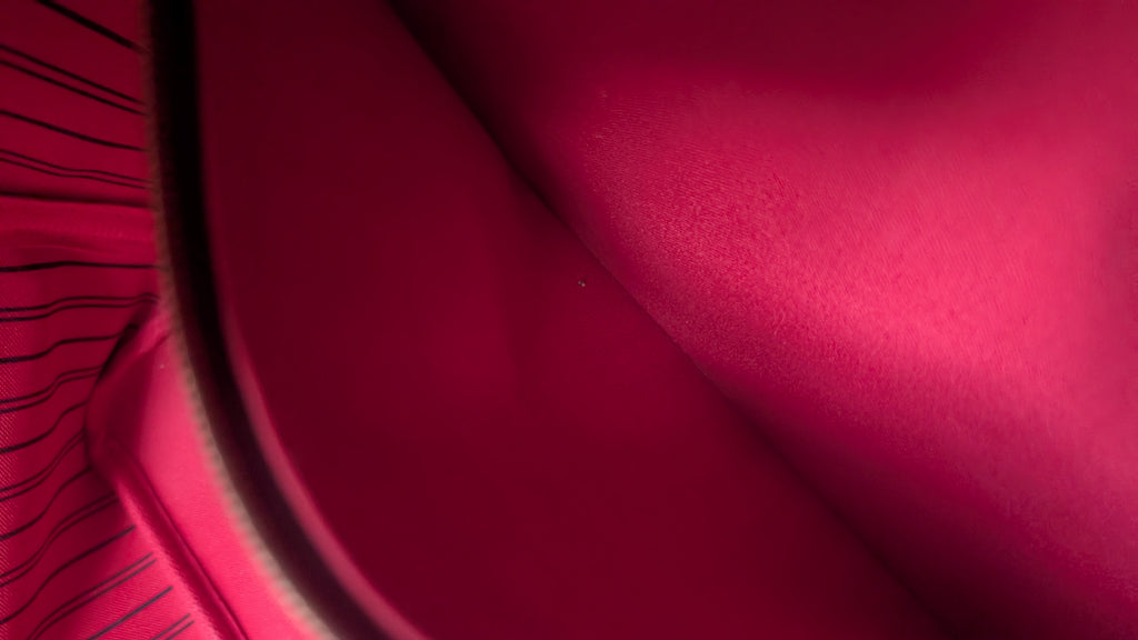 A close-up of a vibrant magenta pink fabric surface with a soft sheen, showing a curved fold and a striped textile detail on the left edge. Pre-Owned Louis Vuitton Neverfull MM Damier Ebene, Cerise Red
