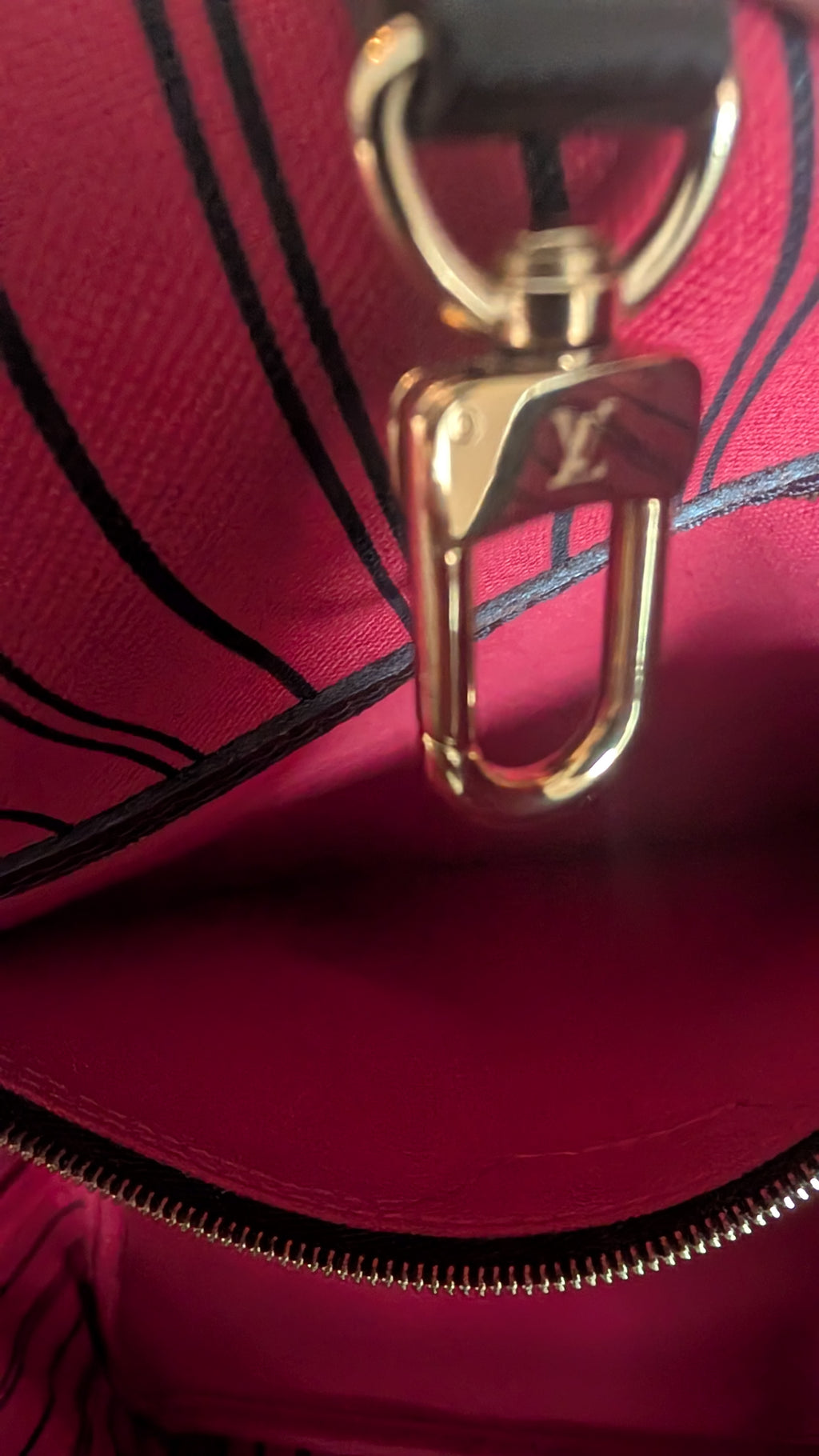Close-up of a Louis Vuitton handbag interior showing a deep magenta-pink lining, black piping details, and a prominent gold-tone metal clasp with the embossed LV logo. Pre-Owned Louis Vuitton Neverfull MM Damier Ebene, Cerise Red