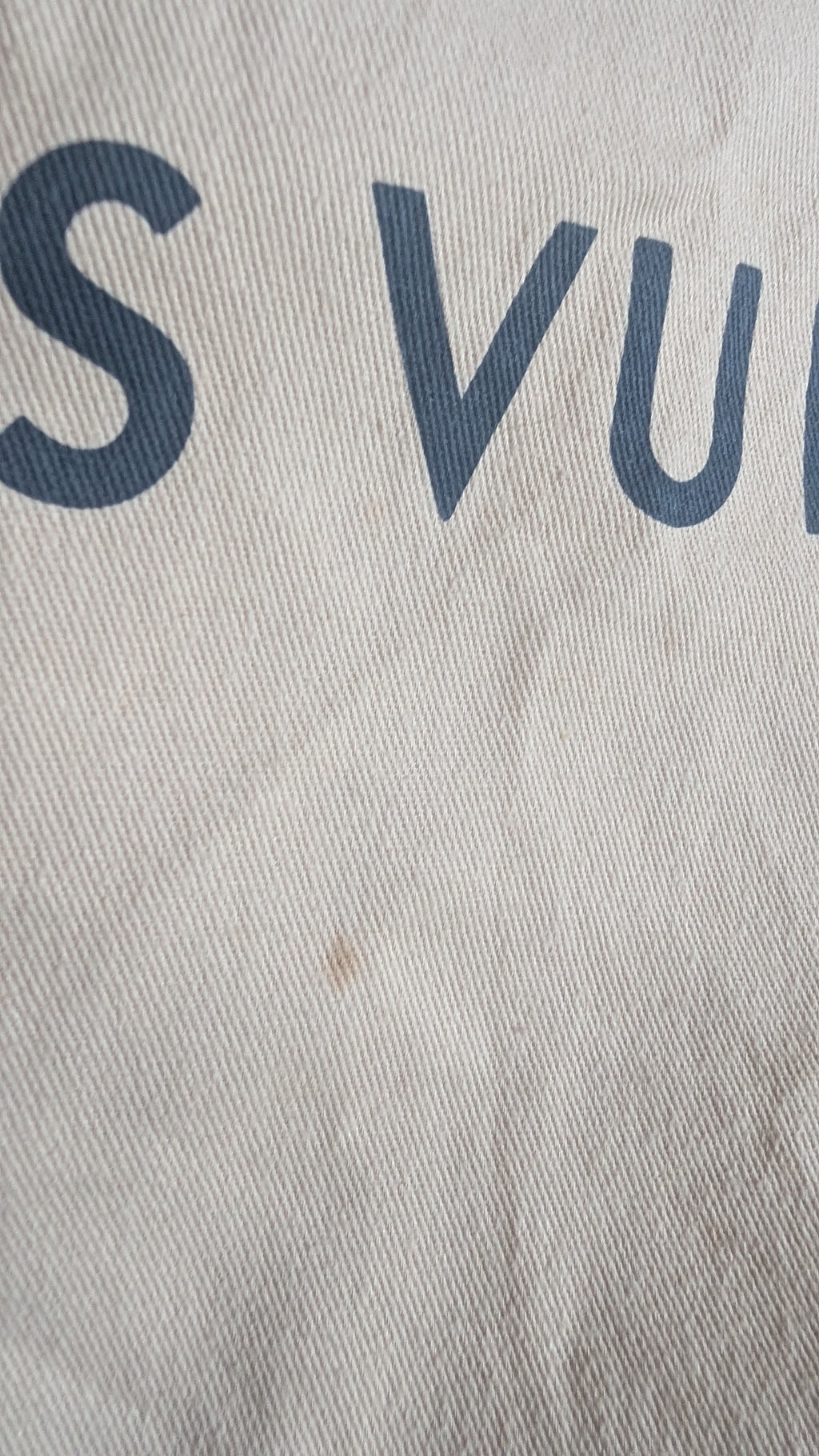 Close-up of a light beige or off-white woven fabric with dark navy blue printed letters, showing part of the text 'S VU'. Pre-Owned Louis Vuitton Neverfull MM Damier Ebene, Cerise Red Pre-Owned Louis Vuitton Neverfull MM Damier Ebene, Cerise Red