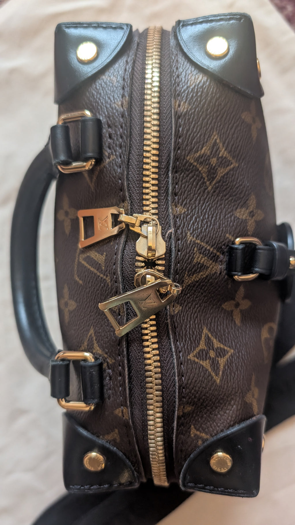 A close-up of a Louis Vuitton monogram handbag in brown coated canvas with black leather trim, gold-tone hardware, and a front zipper closure. Pre-Owned Louis Vuitton Petite Malle Souple Monogram Bag