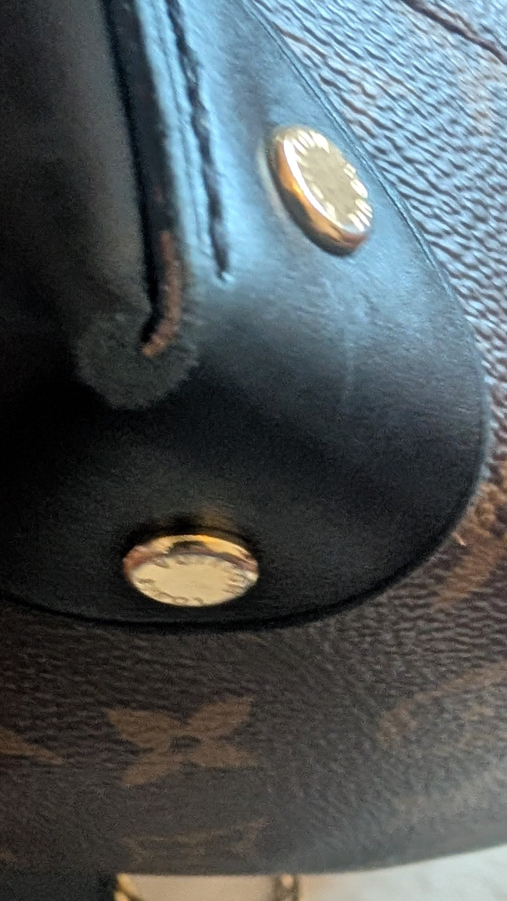 Close-up of a Louis Vuitton monogram shoulder bag in dark brown coated canvas with black leather trim and gold-tone hardware, held by a hand. Pre-Owned Louis Vuitton Petite Malle Souple Monogram Bag