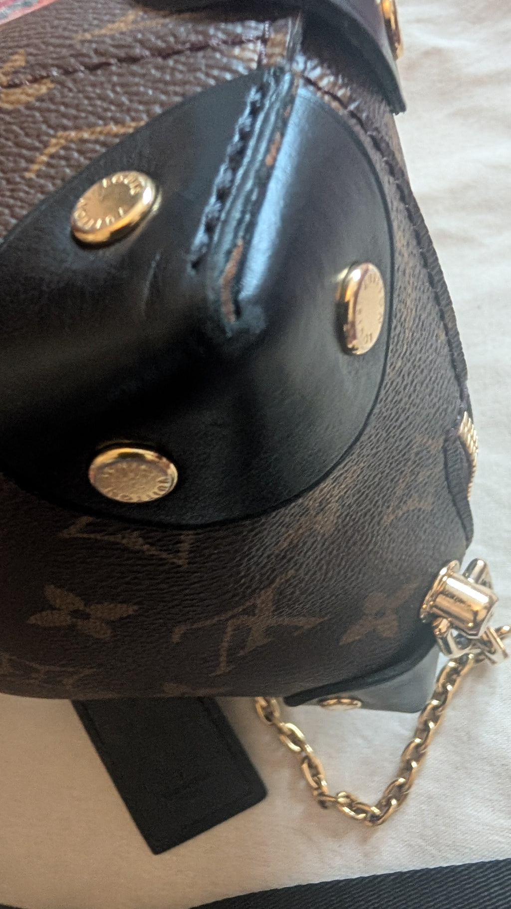 Close-up of a Louis Vuitton monogram shoulder bag with black leather trim and gold-tone hardware, including a chain strap and round metal studs. Pre-Owned Louis Vuitton Petite Malle Souple Monogram Bag