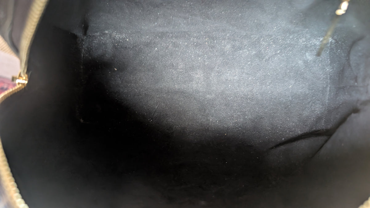 Close-up view of the interior lining of a dark gray or black handbag, showing a textured fabric surface with a gold zipper pull visible on the left edge. Pre-Owned Louis Vuitton Petite Malle Souple Monogram Bag