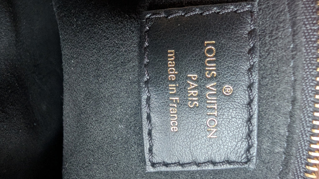 Close-up of a black leather Louis Vuitton patch with gold lettering reading 'LOUIS VUITTON PARIS made in France' on a dark textured background. Pre-Owned Louis Vuitton Petite Malle Souple Monogram Bag