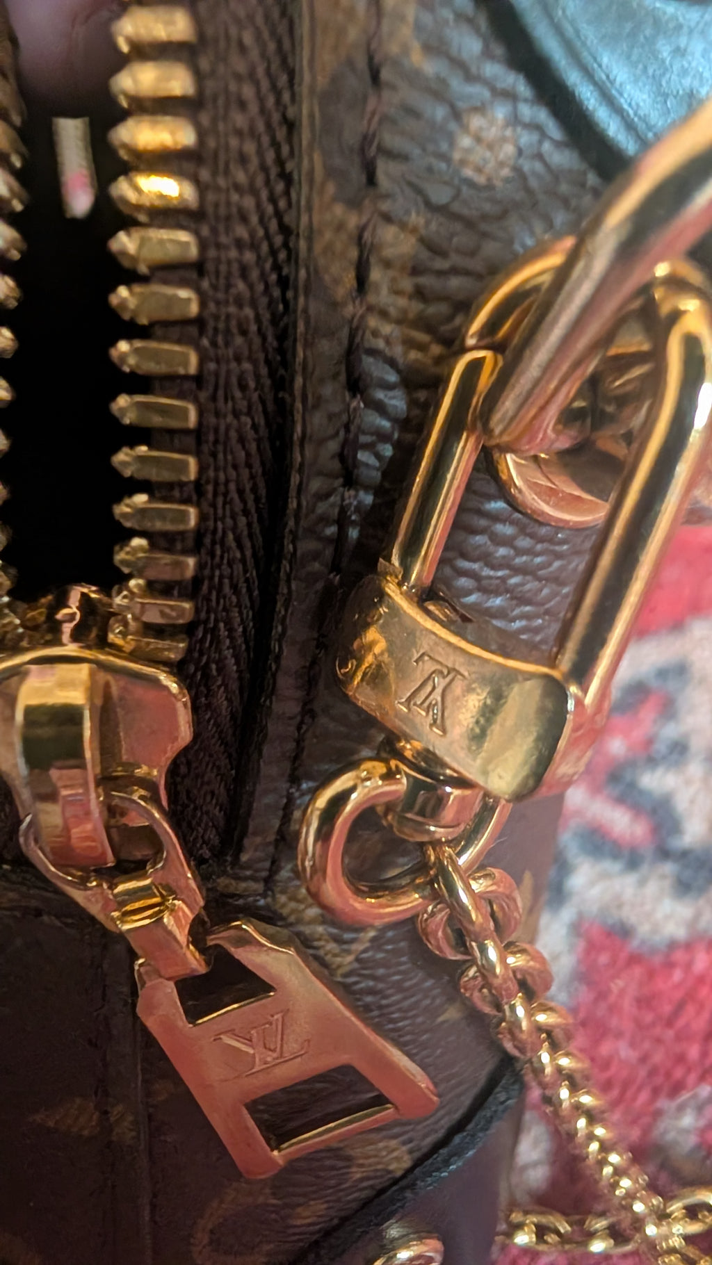 Close-up of a Louis Vuitton monogram handbag showing gold-tone hardware, a zipper pull with an LV logo, and a lock clasp on dark brown coated canvas. Pre-Owned Louis Vuitton Petite Malle Souple Monogram Bag
