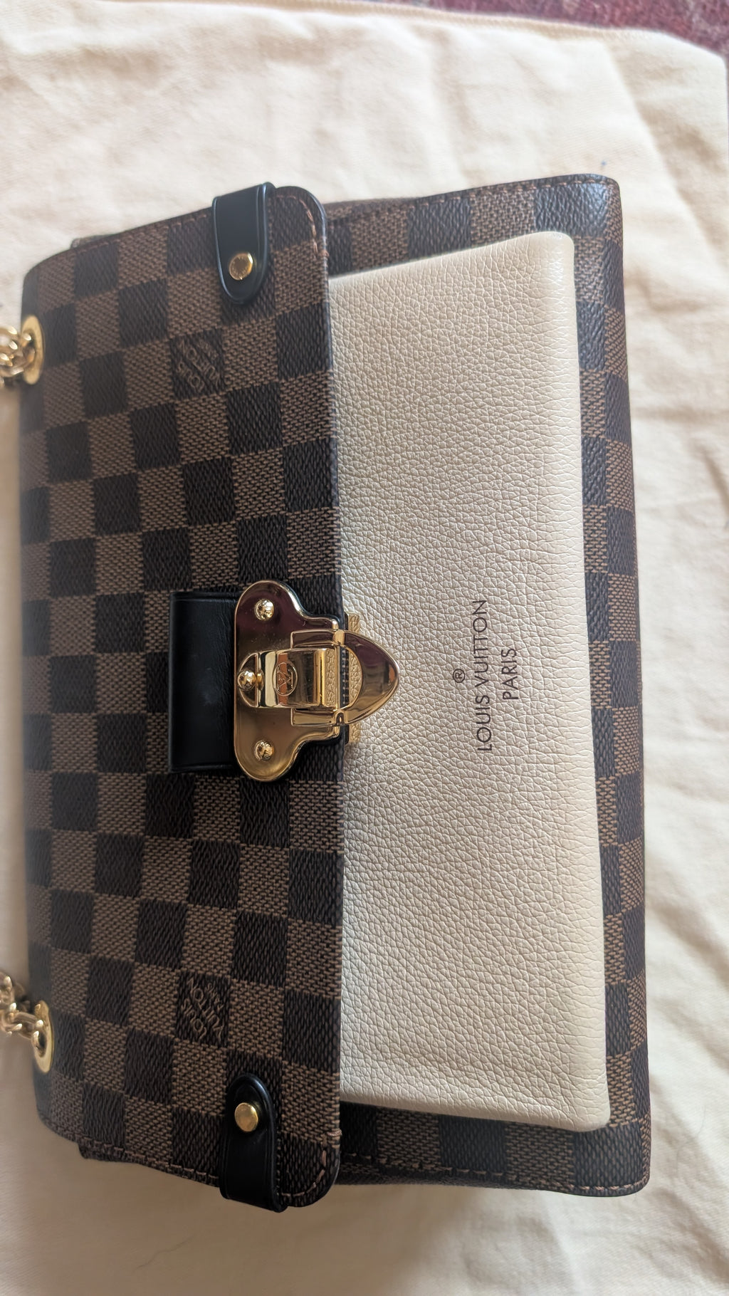 A Louis Vuitton wallet in the Damier Ebene checkered canvas and cream leather combination, featuring a gold-tone clasp and the Louis Vuitton logo embossed on the front, resting on a light fabric background. Pre-Owned Louis Vuitton Vavin PM Damier Ebene / Crème – N40113