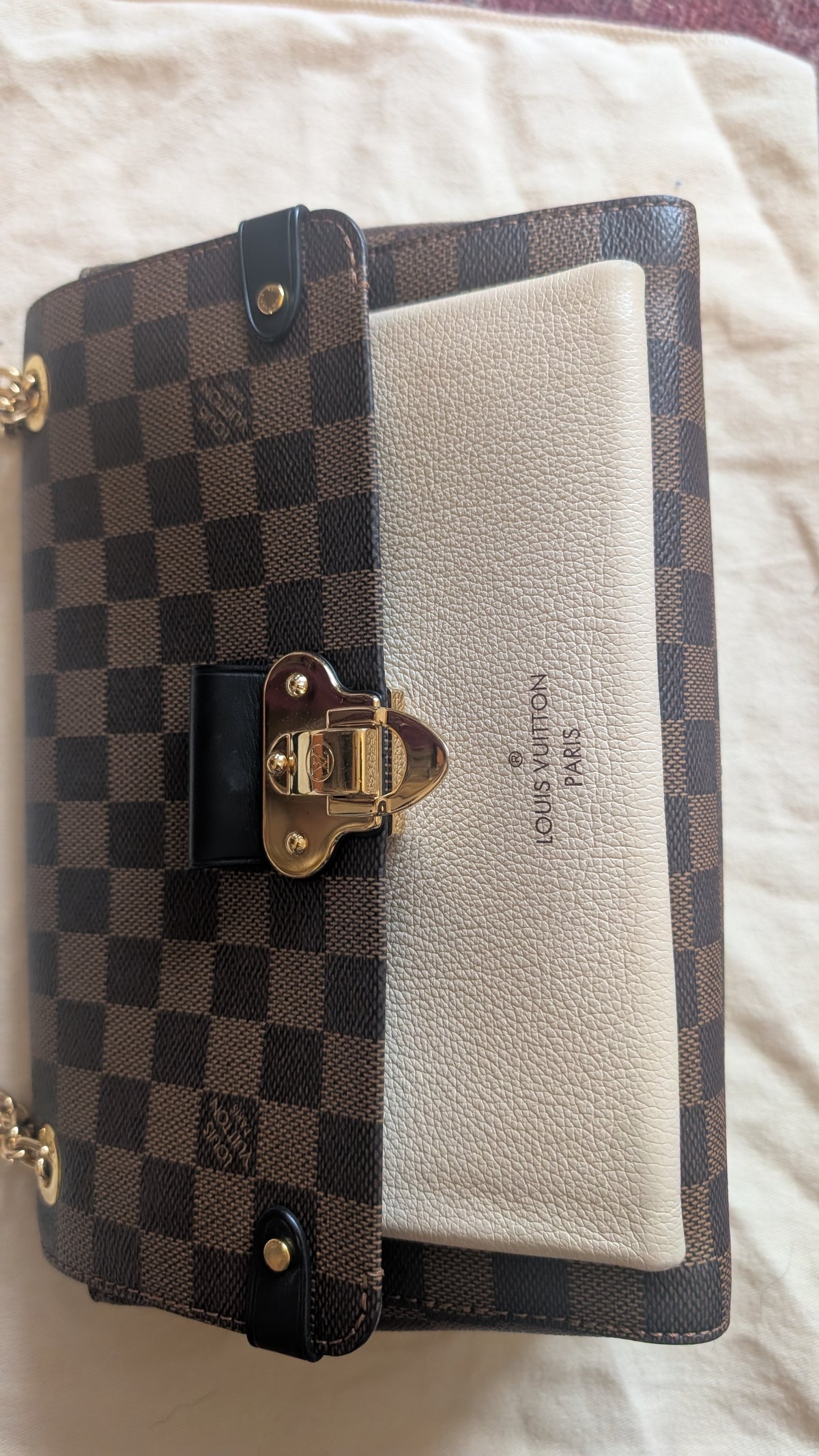 A Louis Vuitton wallet in the Damier Ebene checkered canvas and cream leather combination, featuring a gold-tone clasp and the Louis Vuitton logo embossed on the front, resting on a light fabric background. Pre-Owned Louis Vuitton Vavin PM Damier Ebene / Crème – N40113