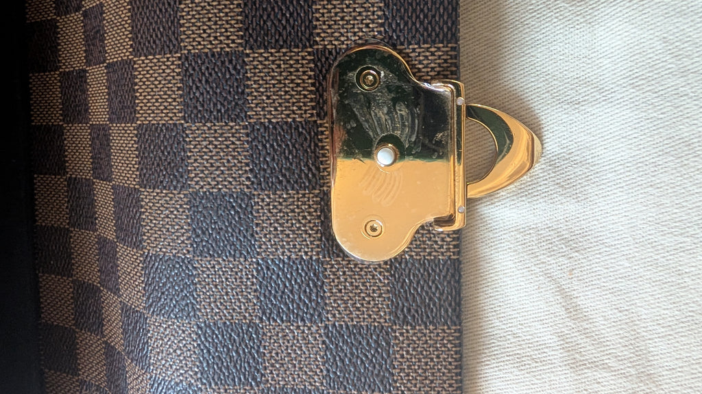 Close-up of a Louis Vuitton Damier Ebene canvas bag with its signature dark brown and beige checkerboard pattern, featuring a polished gold-tone metal clasp. Pre-Owned Louis Vuitton Vavin PM Damier Ebene / Crème – N40113