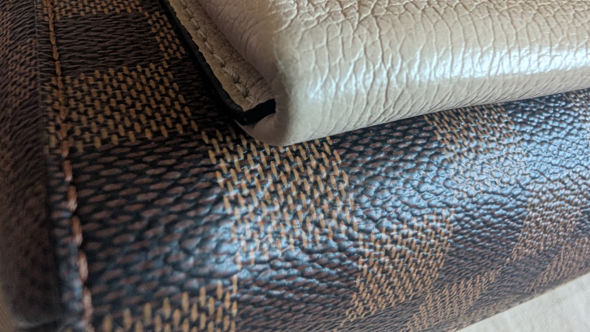 Close-up of a textured leather wallet or clutch showing a dark brown and beige checkered patterned surface with a folded light beige leather section. Pre-Owned Louis Vuitton Vavin PM Damier Ebene / Crème – N40113