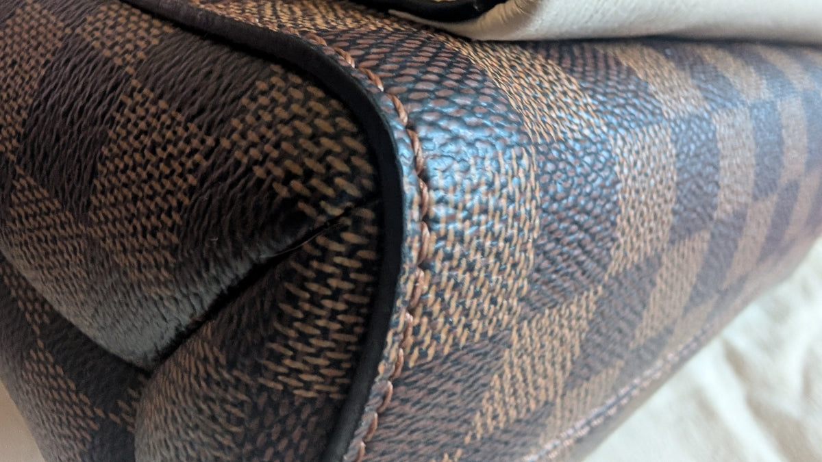 Close-up of a brown and beige checkered patterned leather or faux leather product corner with black edging and visible stitching. Pre-Owned Louis Vuitton Vavin PM Damier Ebene / Crème – N40113