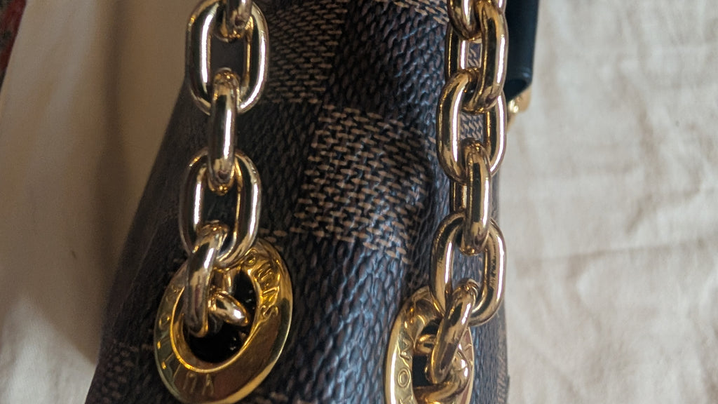 Close-up of a dark brown and beige checkered handbag with a chunky gold chain strap and a gold-tone circular metal charm. Pre-Owned Louis Vuitton Vavin PM Damier Ebene / Crème – N40113