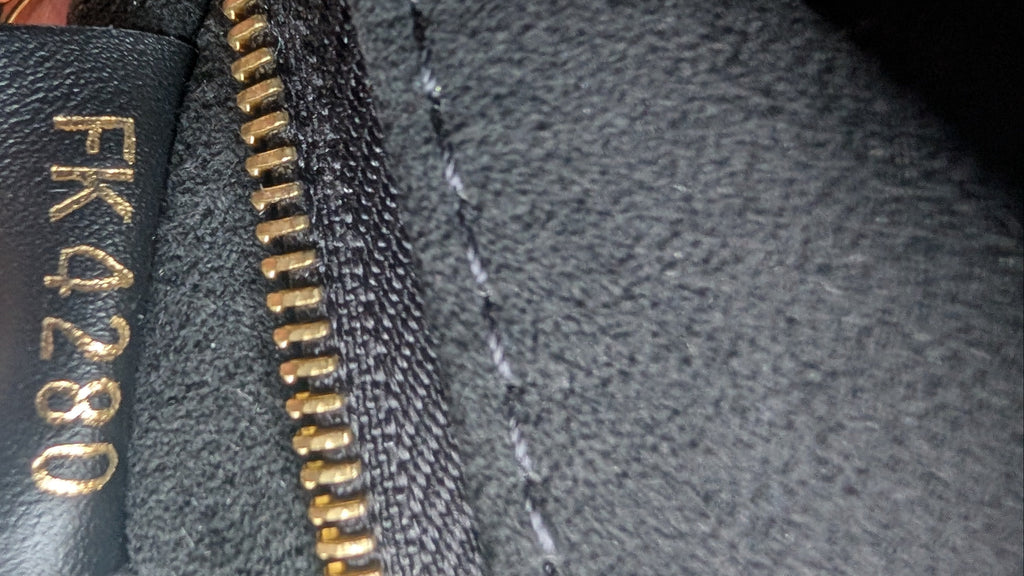 Close-up of a black leather interior label with gold lettering reading 'FK4280' next to a gold zipper on dark gray fabric, with a finger holding it. Pre-Owned Louis Vuitton Vavin PM Damier Ebene / Crème – N40113