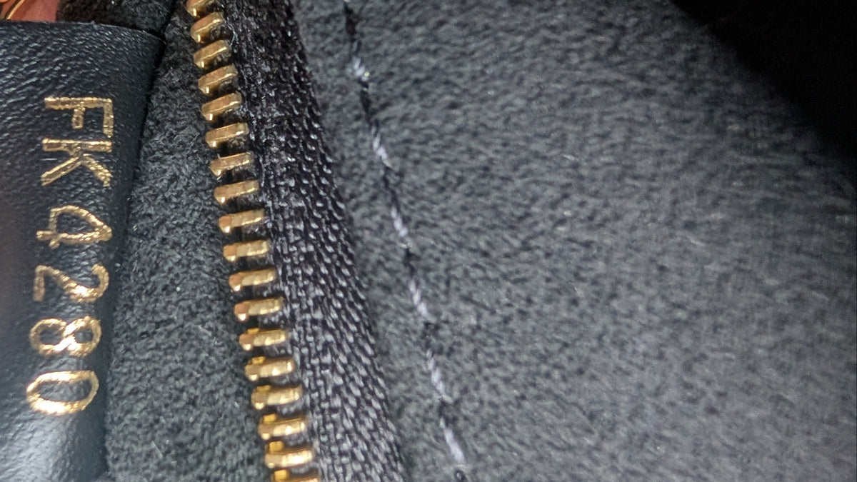 Close-up of a black leather interior label with gold lettering reading 'FK4280' next to a gold zipper on dark gray fabric, with a finger holding it. Pre-Owned Louis Vuitton Vavin PM Damier Ebene / Crème – N40113