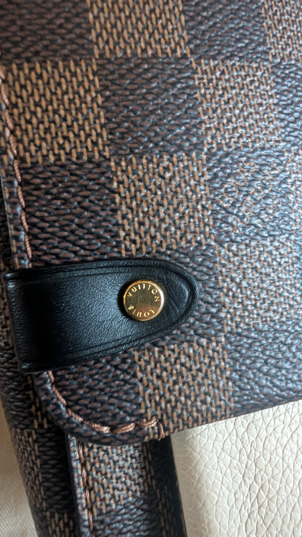 Close-up of a Louis Vuitton monogram bag featuring the Damier Ebene pattern in brown and beige, with a black leather strap and a gold-tone circular metal snap button. Pre-Owned Louis Vuitton Vavin PM Damier Ebene / Crème – N40113