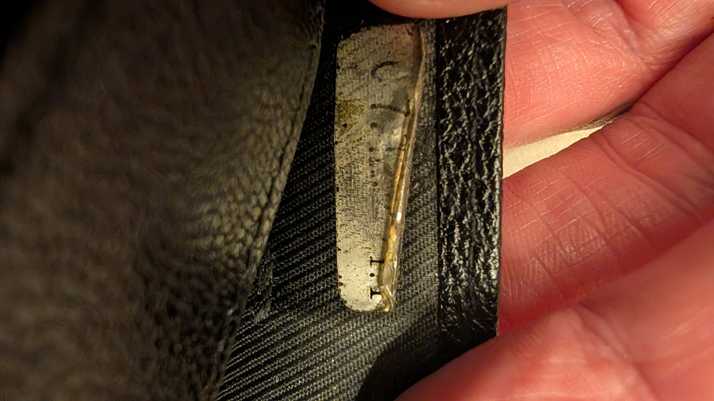 A close-up of a black textured leather or faux-leather item being held by a hand, showing a worn, frayed, and damaged section of the material with exposed inner layers. Pre-Owned Chanel Vintage Black Caviar Leather Wallet with Added Chain