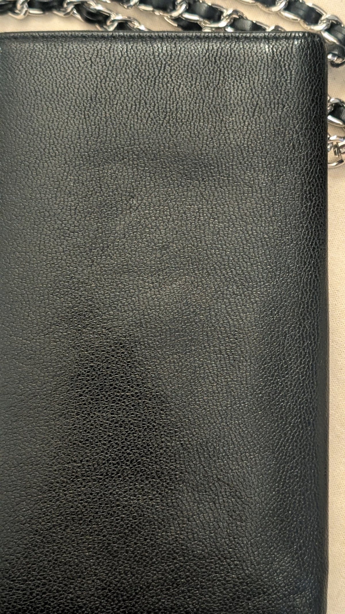 Close-up of a black pebbled leather item, likely a clutch or wallet, with a silver chain strap visible along the top edge. Pre-Owned Chanel Vintage Black Caviar Leather Wallet with Added Chain