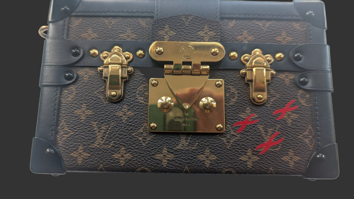 A Louis Vuitton monogram canvas trunk bag with black leather trim, gold-tone hardware, and red paint markings on the front, photographed from a top-down angle on a white background. Pre-Owned Louis Vuitton Petite Malle Monogram Canvas Crossbody Bag