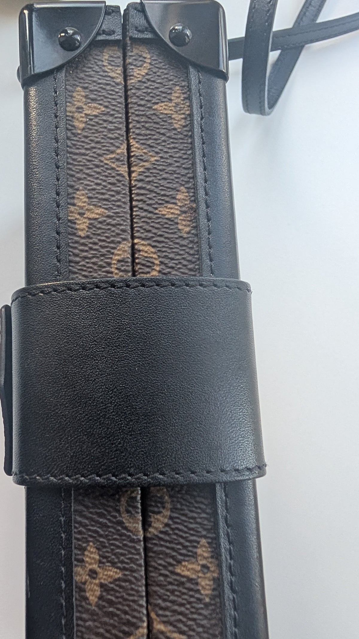 A close-up of a Louis Vuitton monogram canvas and leather strap accessory, likely a pouch or strap component, featuring the classic brown monogram pattern and a black leather strap closure. Pre-Owned Louis Vuitton Petite Malle Monogram Canvas Crossbody Bag