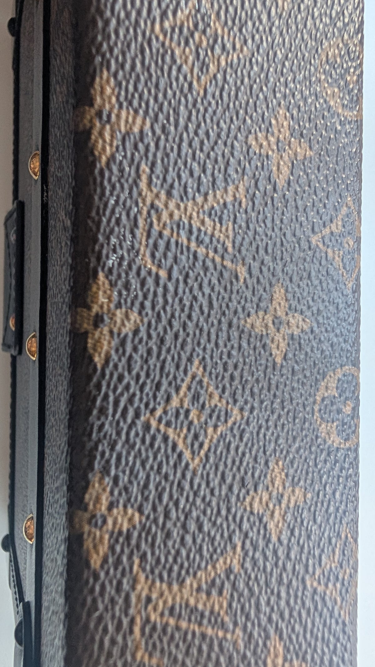 Close-up of a Louis Vuitton monogram canvas surface, showing the classic brown and tan LV pattern with gold-tone hardware visible along the left edge. Pre-Owned Louis Vuitton Petite Malle Monogram Canvas Crossbody Bag