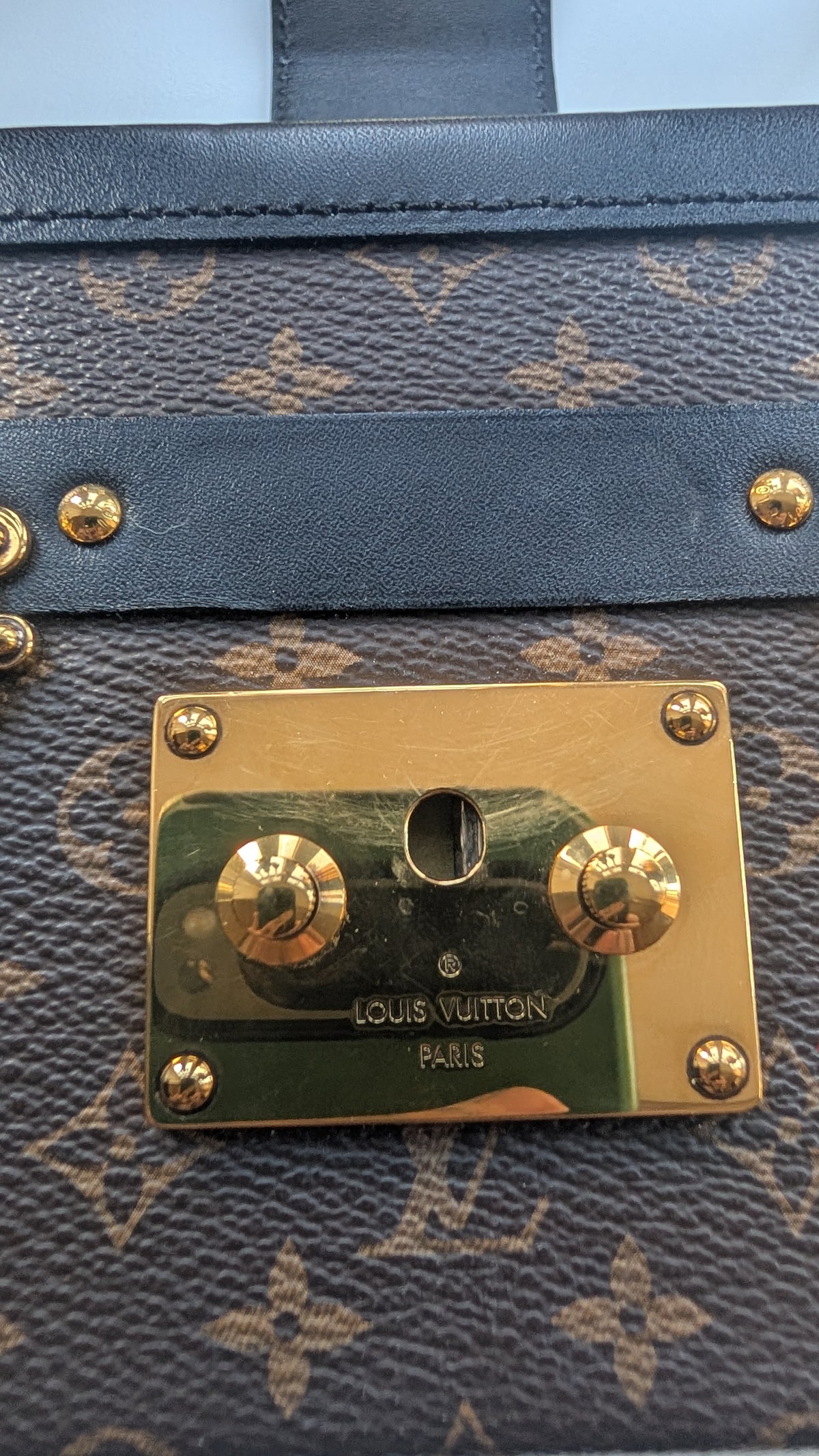 Close-up of a Louis Vuitton monogram bag with dark blue leather trim and a gold-tone metal clasp on a brown monogram canvas. Pre-Owned Louis Vuitton Petite Malle Monogram Canvas Crossbody Bag