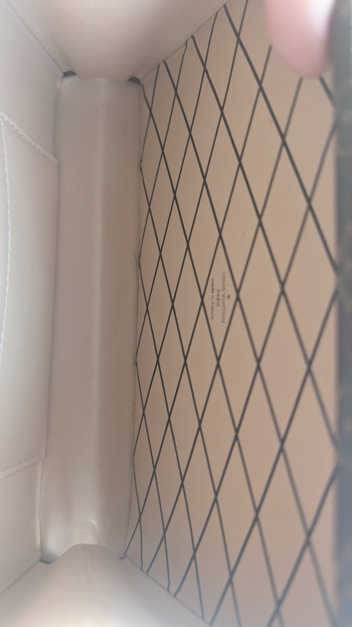 Close-up of the interior of a light beige or off-white handbag, showing a diamond-patterned lining with a small printed logo in the center. Pre-Owned Louis Vuitton Petite Malle Monogram Canvas Crossbody Bag