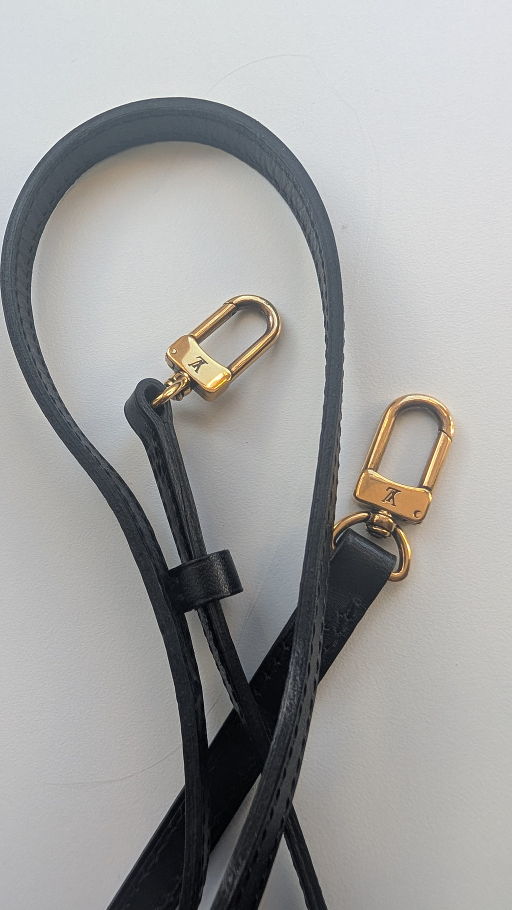 A black leather strap accessory with gold-tone metal swivel clasp hardware, laid out on a light gray background. Pre-Owned Louis Vuitton Petite Malle Monogram Canvas Crossbody Bag