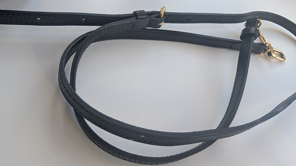 A black leather strap, likely a saddle pad or horse accessory, featuring gold-tone metal hardware, coiled on a plain white surface. Pre-Owned Louis Vuitton Petite Malle Monogram Canvas Crossbody Bag