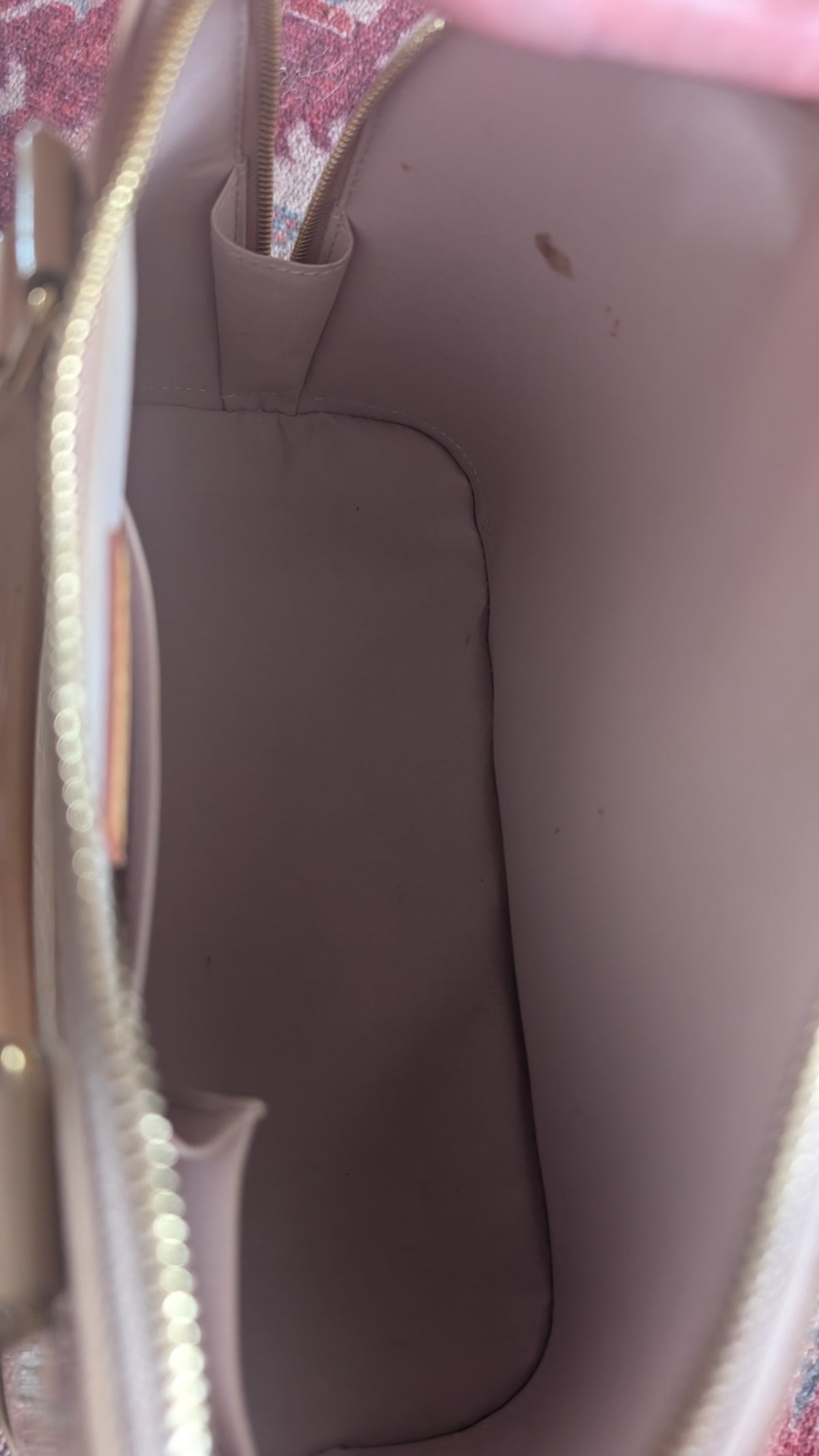Close-up view of the interior lining of a handbag in a muted taupe-brown color, showing the inside walls, a zipper track, and a small side pocket. Pre-Owned Louis Vuitton Alma PM Monogram Vernis – Beige Poudre