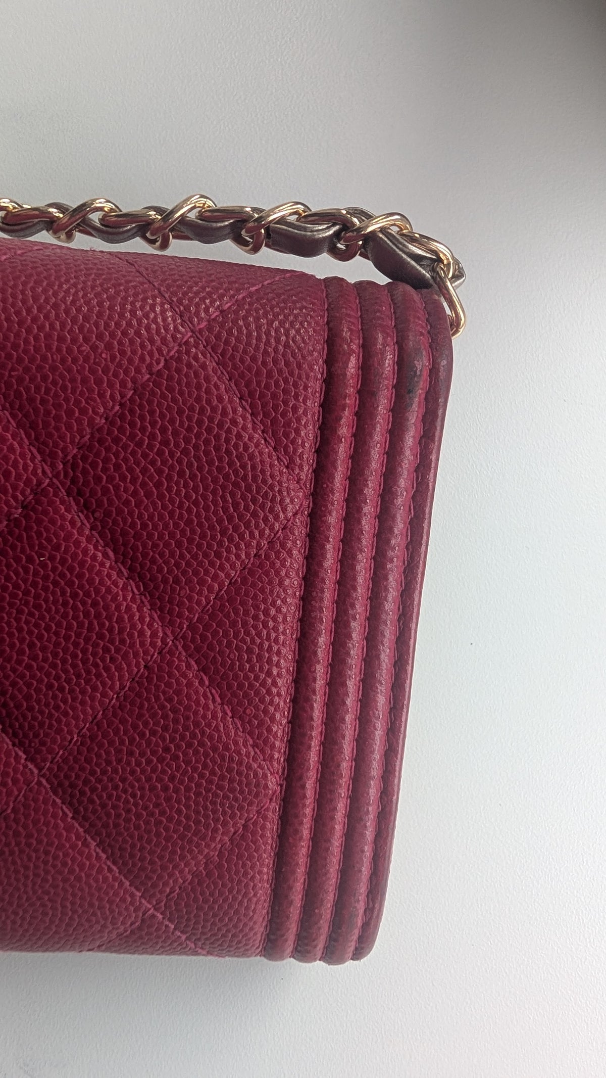 A close-up of a quilted leather shoulder bag in deep burgundy, showing the textured grain, diamond quilting, and a gold-tone chain strap against a plain light background. Pre-Owned Chanel Boy Wallet on Chain – Fuchsia Pink Caviar Leather – Gold Hardware