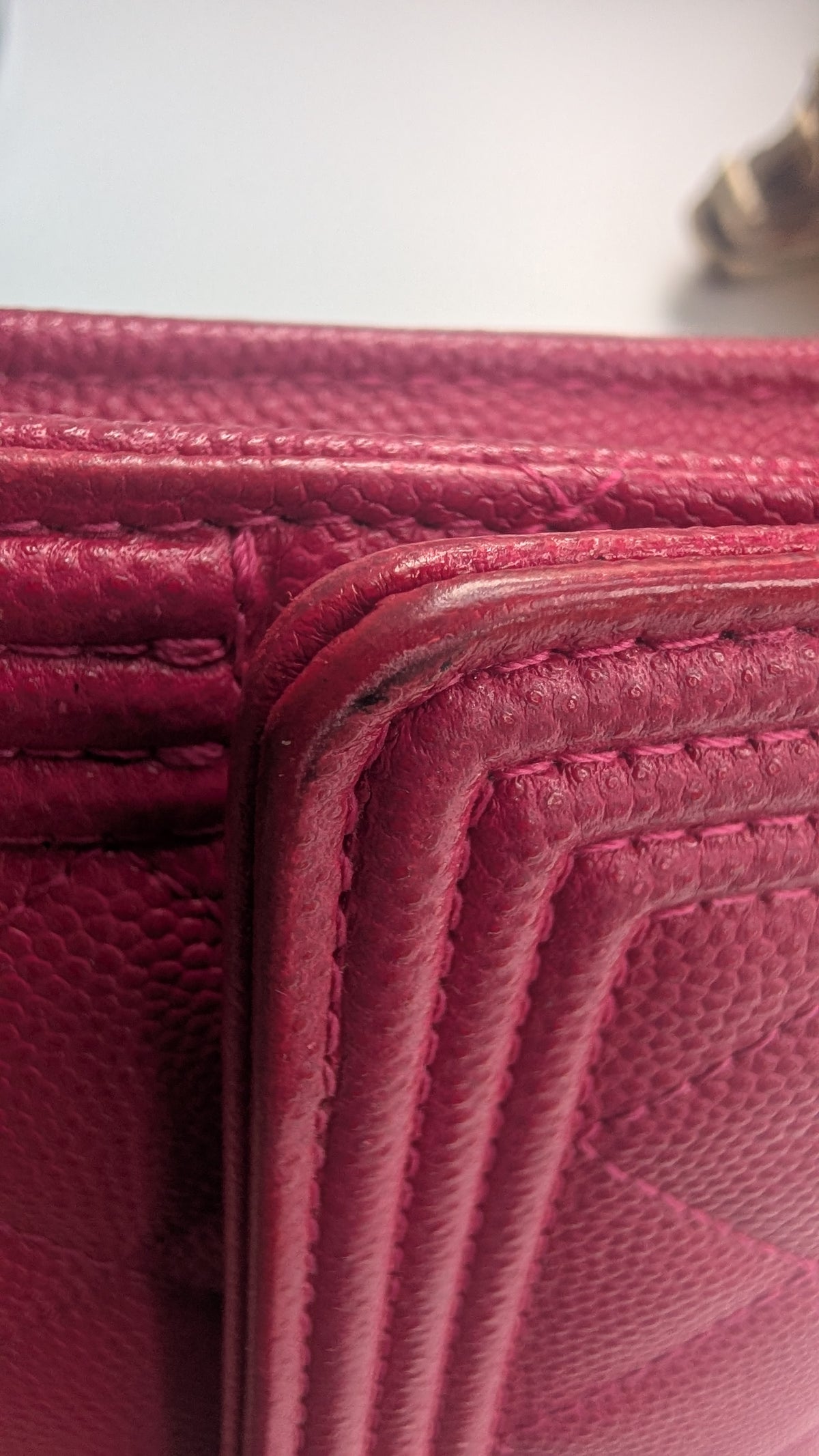 Close-up of a textured pink leather item showing the corner seam and stitching details. Pre-Owned Chanel Boy Wallet on Chain – Fuchsia Pink Caviar Leather – Gold Hardware