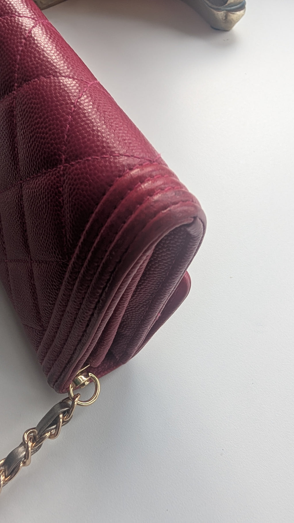 A close-up of a burgundy quilted leather handbag corner with a gold-tone chain strap on a plain light background. Pre-Owned Chanel Boy Wallet on Chain – Fuchsia Pink Caviar Leather – Gold Hardware