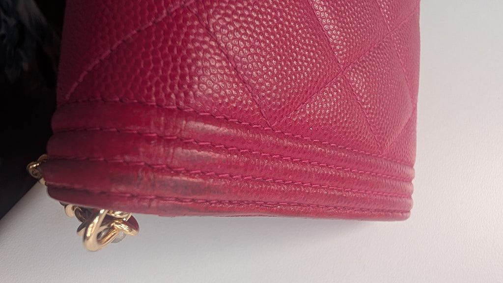 A close-up of a pink quilted leather handbag corner showing the texture, stitching, and a gold-tone metal clasp on a white surface. Pre-Owned Chanel Boy Wallet on Chain – Fuchsia Pink Caviar Leather – Gold Hardware