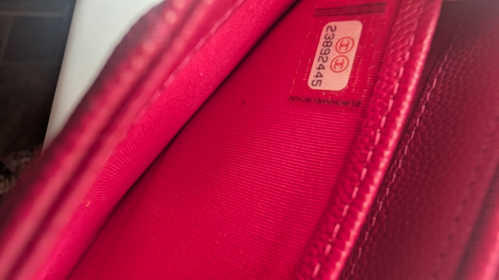 Close-up of a bright pink textured leather interior lining with a small white sticker showing a serial number. Pre-Owned Chanel Boy Wallet on Chain – Fuchsia Pink Caviar Leather – Gold Hardware