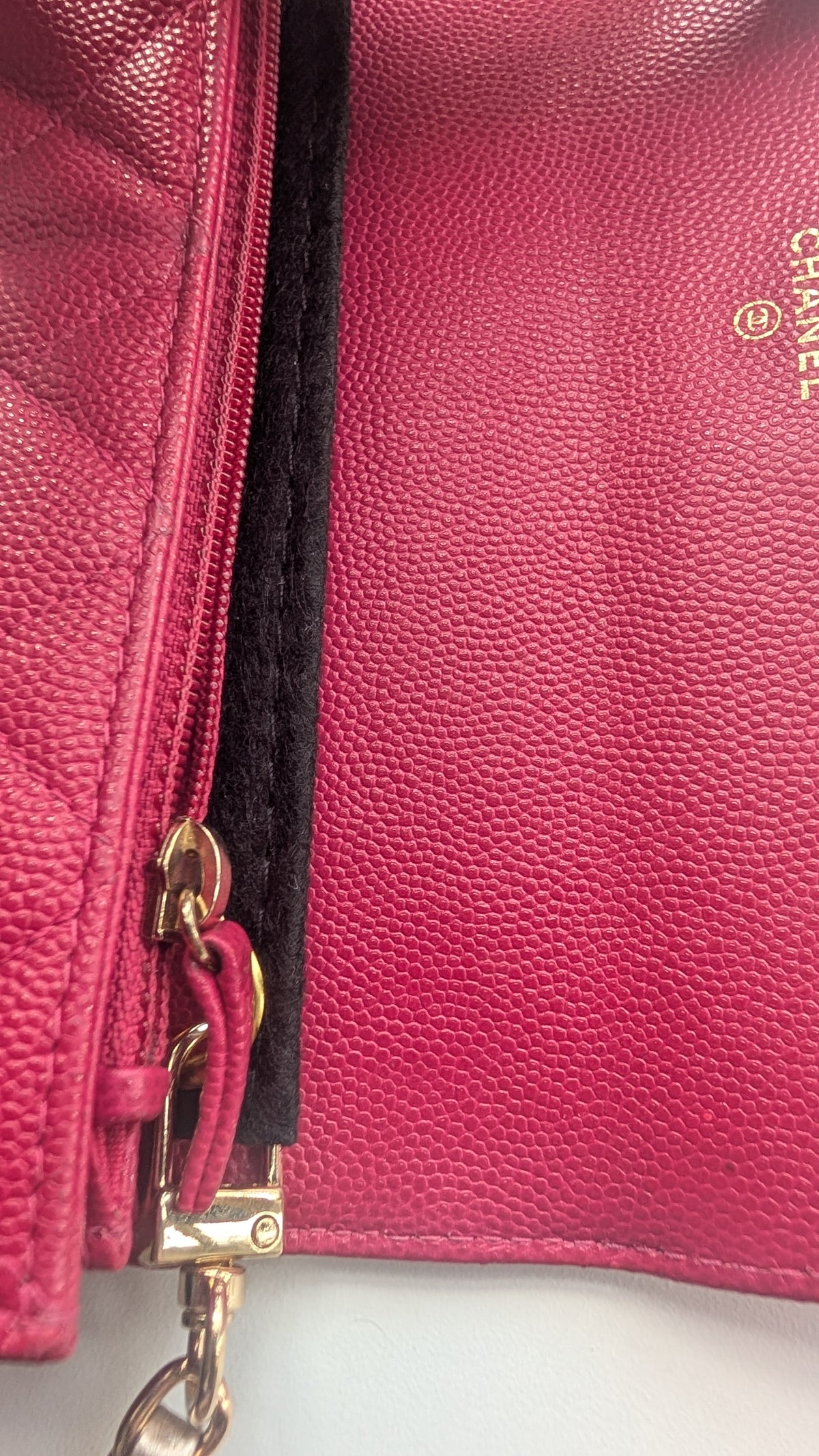 Close-up of a pink pebbled leather Chanel bag with gold hardware, a black zipper track, and a gold Chanel logo on the interior. Pre-Owned Chanel Boy Wallet on Chain – Fuchsia Pink Caviar Leather – Gold Hardware