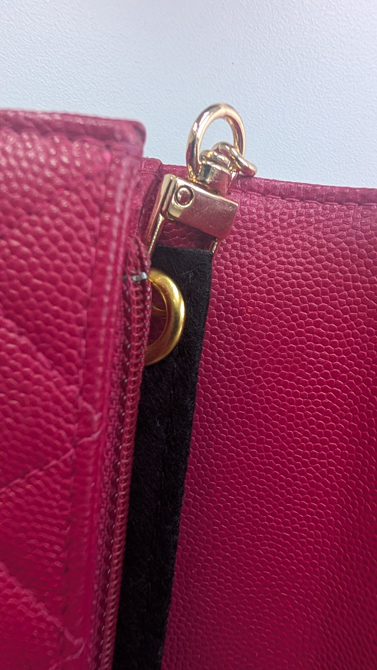 A close-up of a fuchsia pink pebbled leather handbag showing a gold-tone metal clasp and a black fabric strap. Pre-Owned Chanel Boy Wallet on Chain – Fuchsia Pink Caviar Leather – Gold Hardware