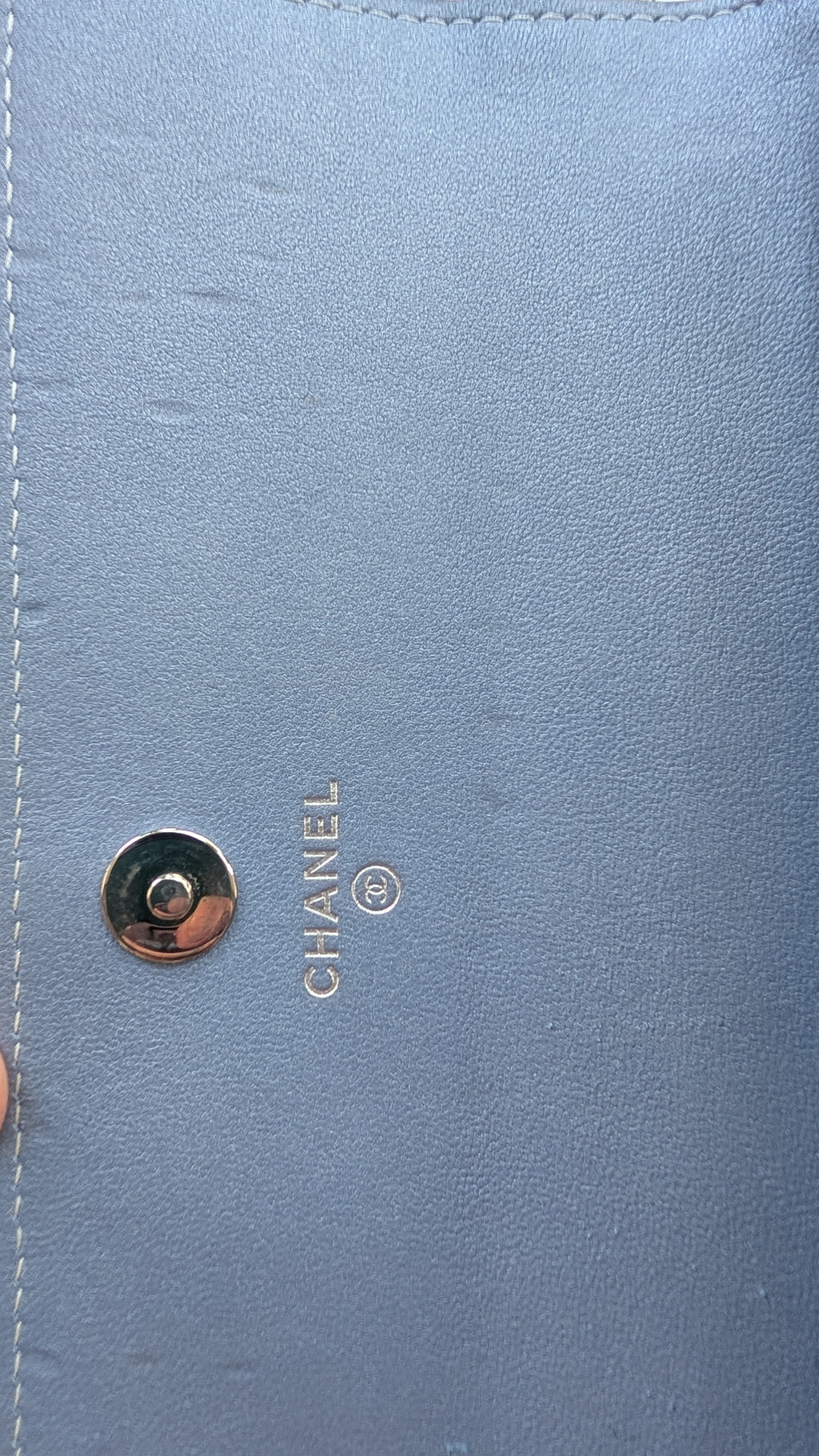 Close-up of a light blue leather Chanel bag with a gold-tone snap button and the embossed CHANEL logo. Pre-Owned Chanel Camellia Studded Wallet on Chain WOC – Blue Lambskin